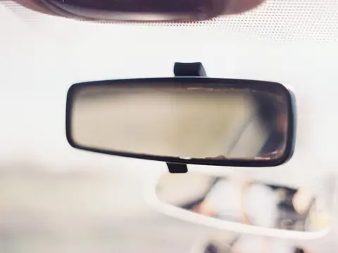 A rear-view mirror on a windshield against a bright white sky