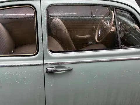 The door window of a pale green car beaded with raindrops, the seats seen through the glass