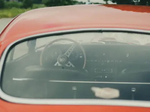 The rear window of a red classic coupe, the steering wheel seen through the glass