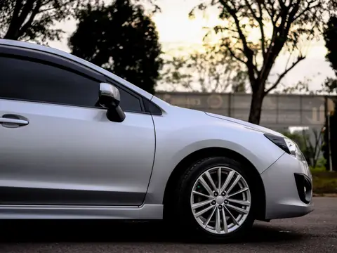 The side windows of a silver hatchback parked under trees at dusk
