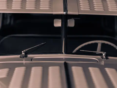 The windshield and chrome wiper arms of a classic car, seen across its louvred bonnet